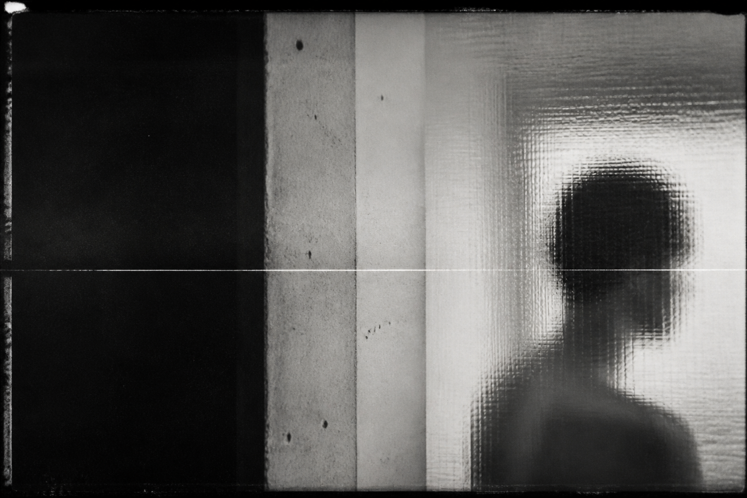 An anonymous figure seen through textured glass in a concrete interior